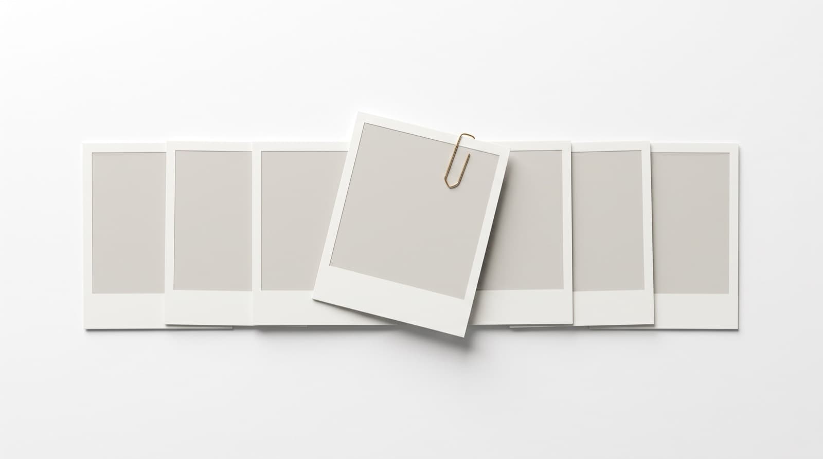 A row of overlapping blank photo prints with one lifted clear under a brass clip