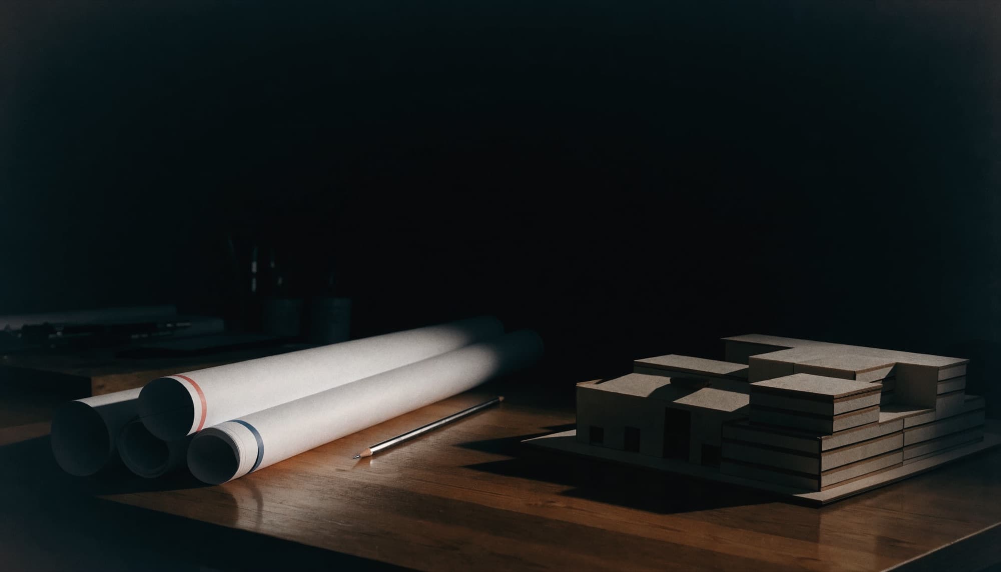 An architect's desk with rolled drawings and a scale model in low light