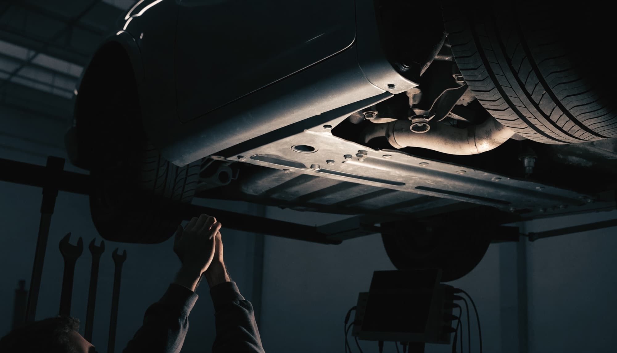 A car on a lift in a workshop bay with the underbody lit by work lights