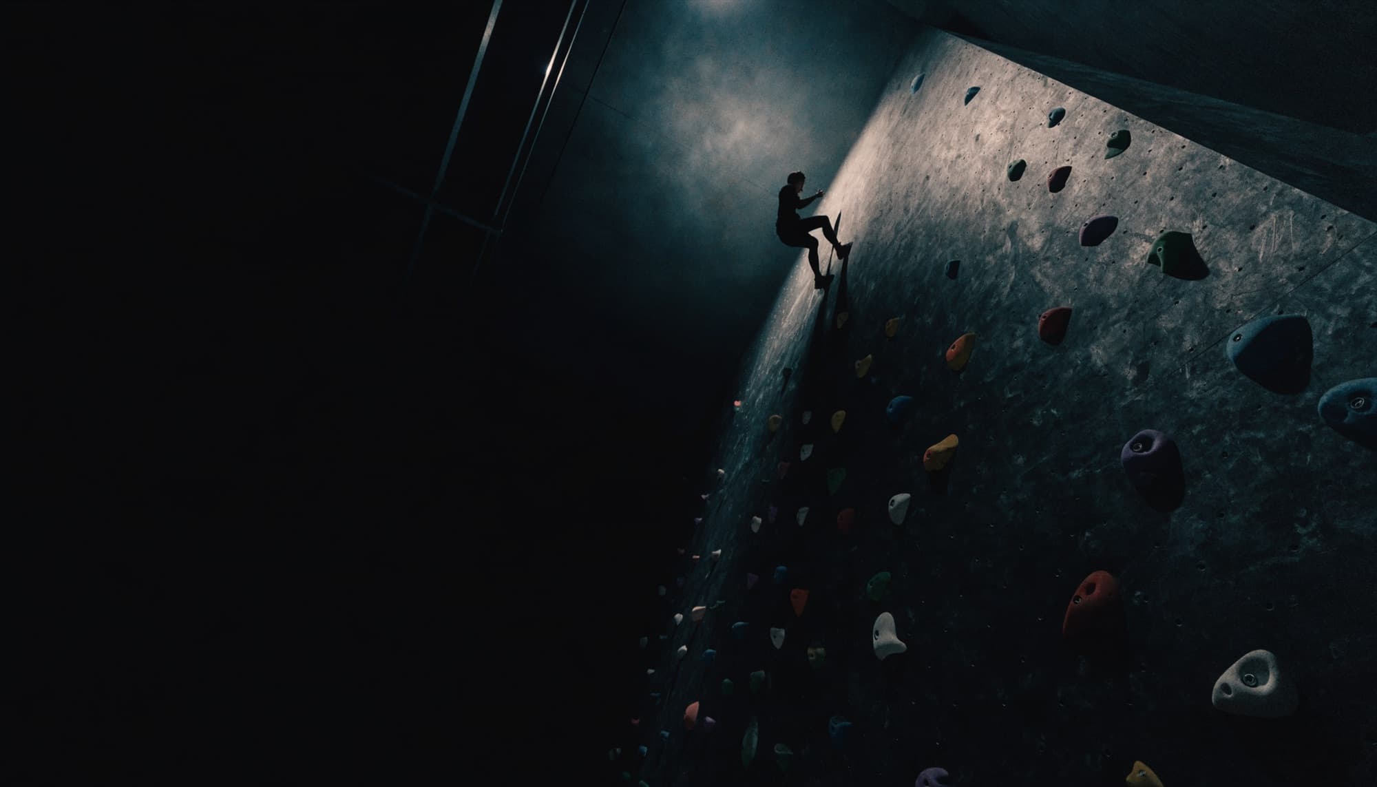 A tall indoor climbing wall photographed from below with a distant climber