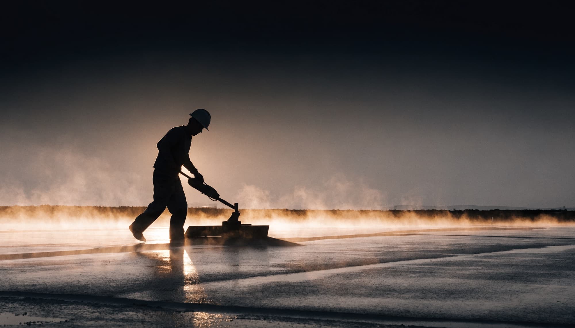 A concrete finisher power-troweling a fresh slab at dawn
