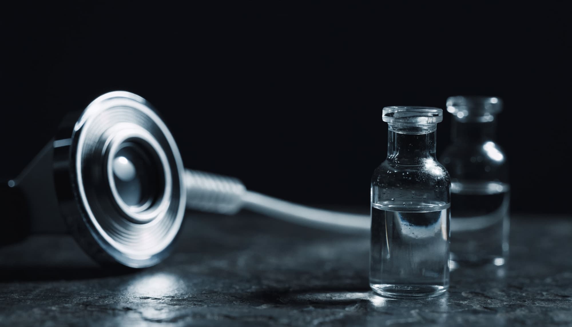 A dermatoscope and clinical skincare vials on a dark stone surface