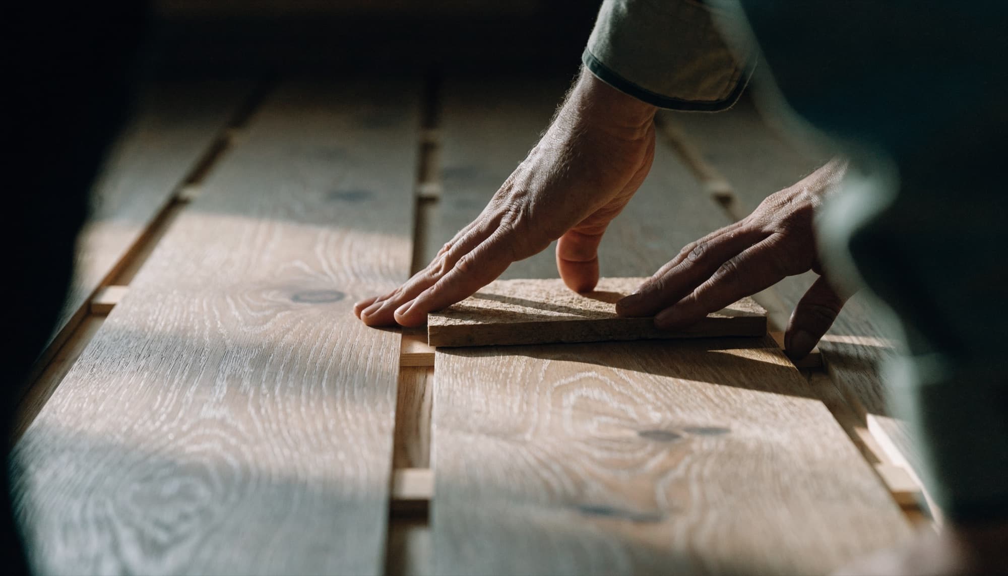 Close crop of hands laying wide-plank engineered timber flooring