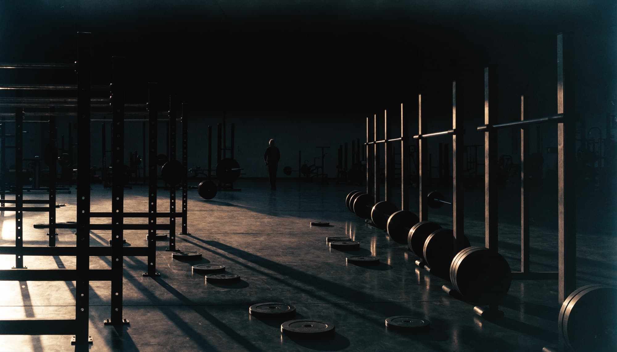 A gym floor at early morning with racks and plates in low raking light