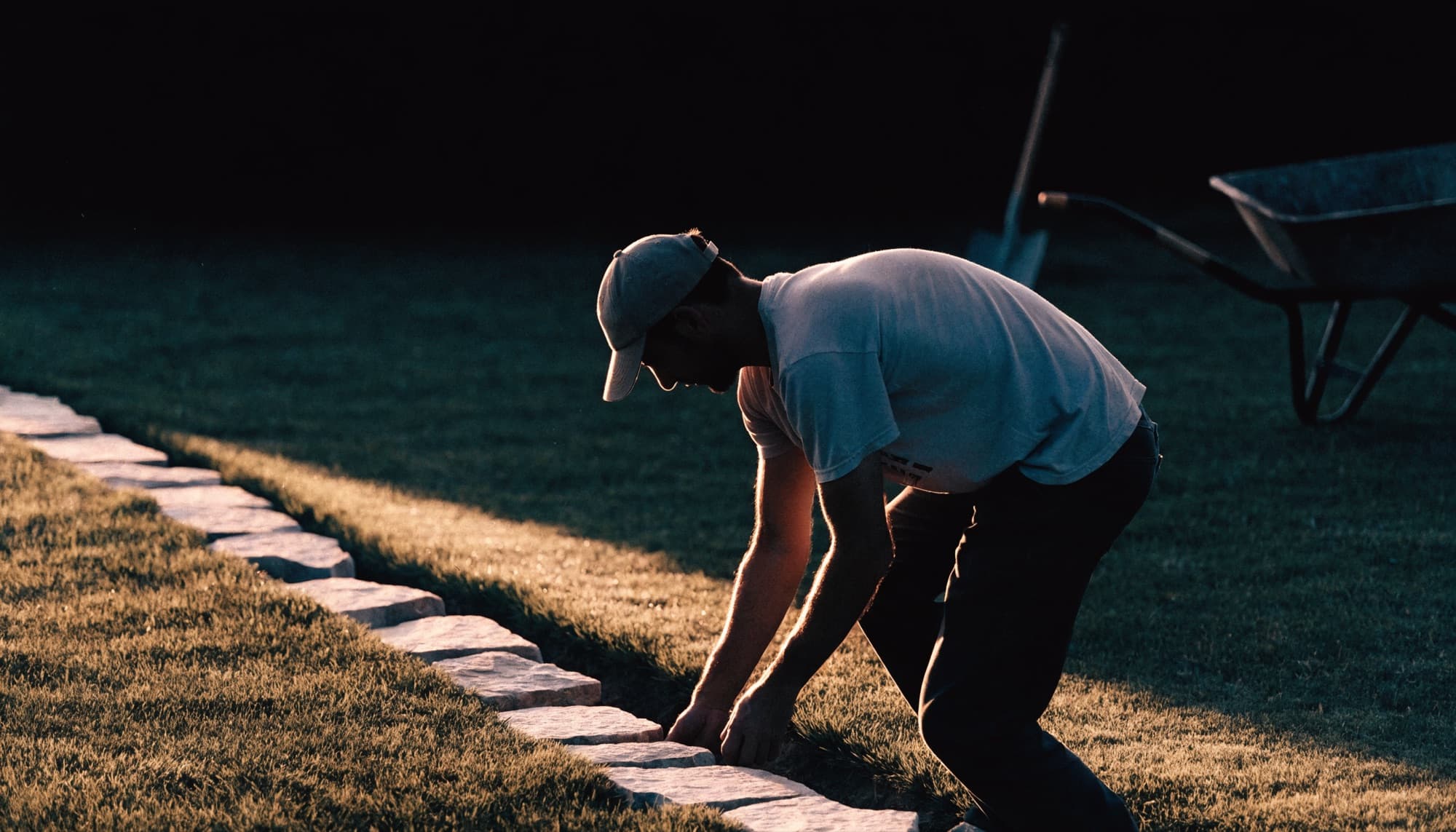 A landscaper laying stone hardscape edging at golden hour