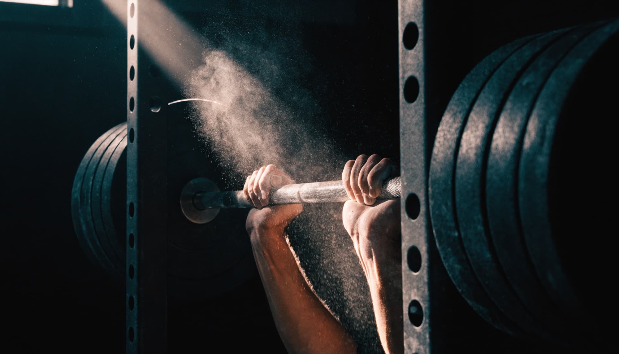 Hands gripping a loaded barbell with chalk dust in a shaft of light