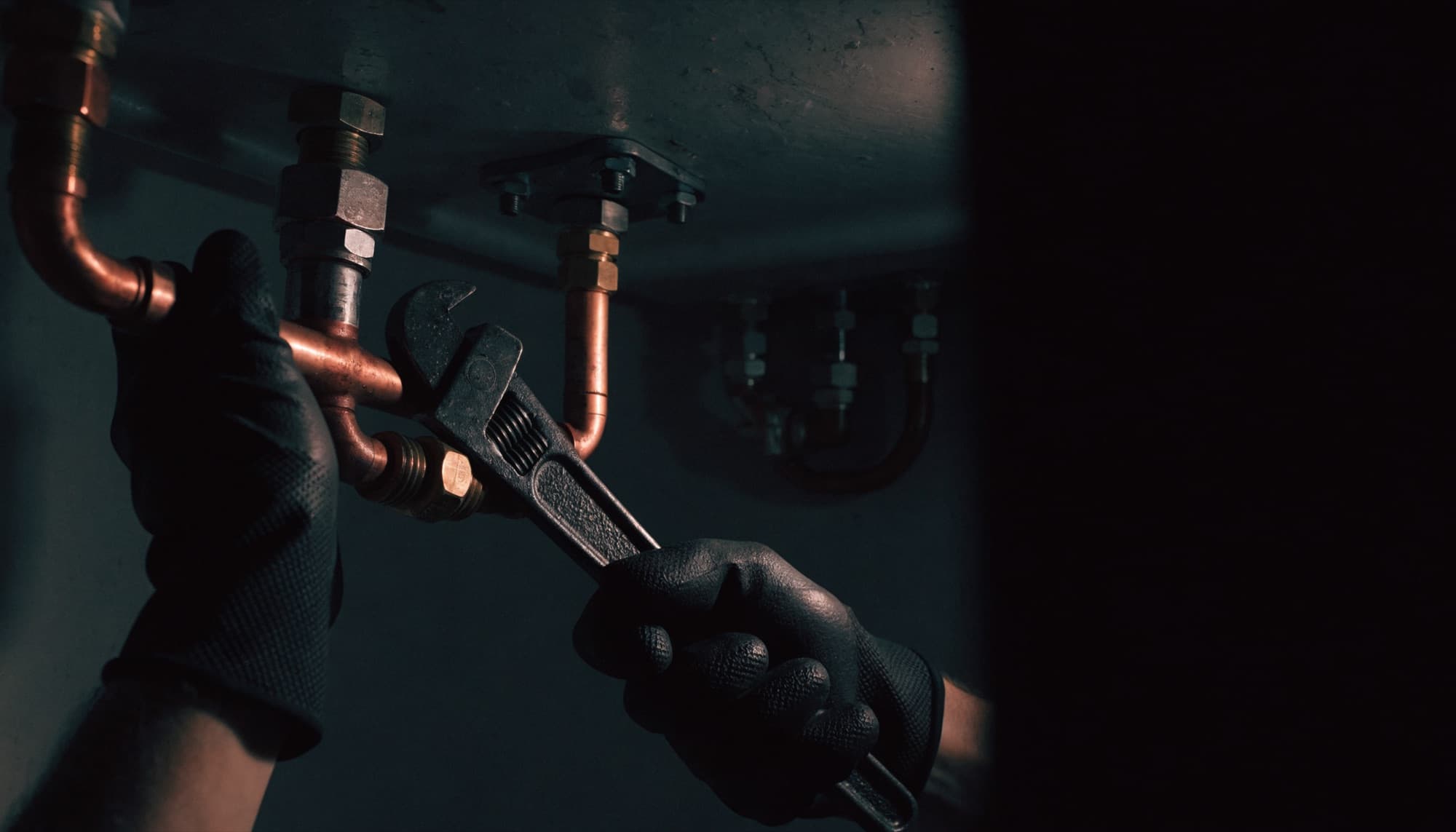 A plumber's hands working on copper pipework under a sink
