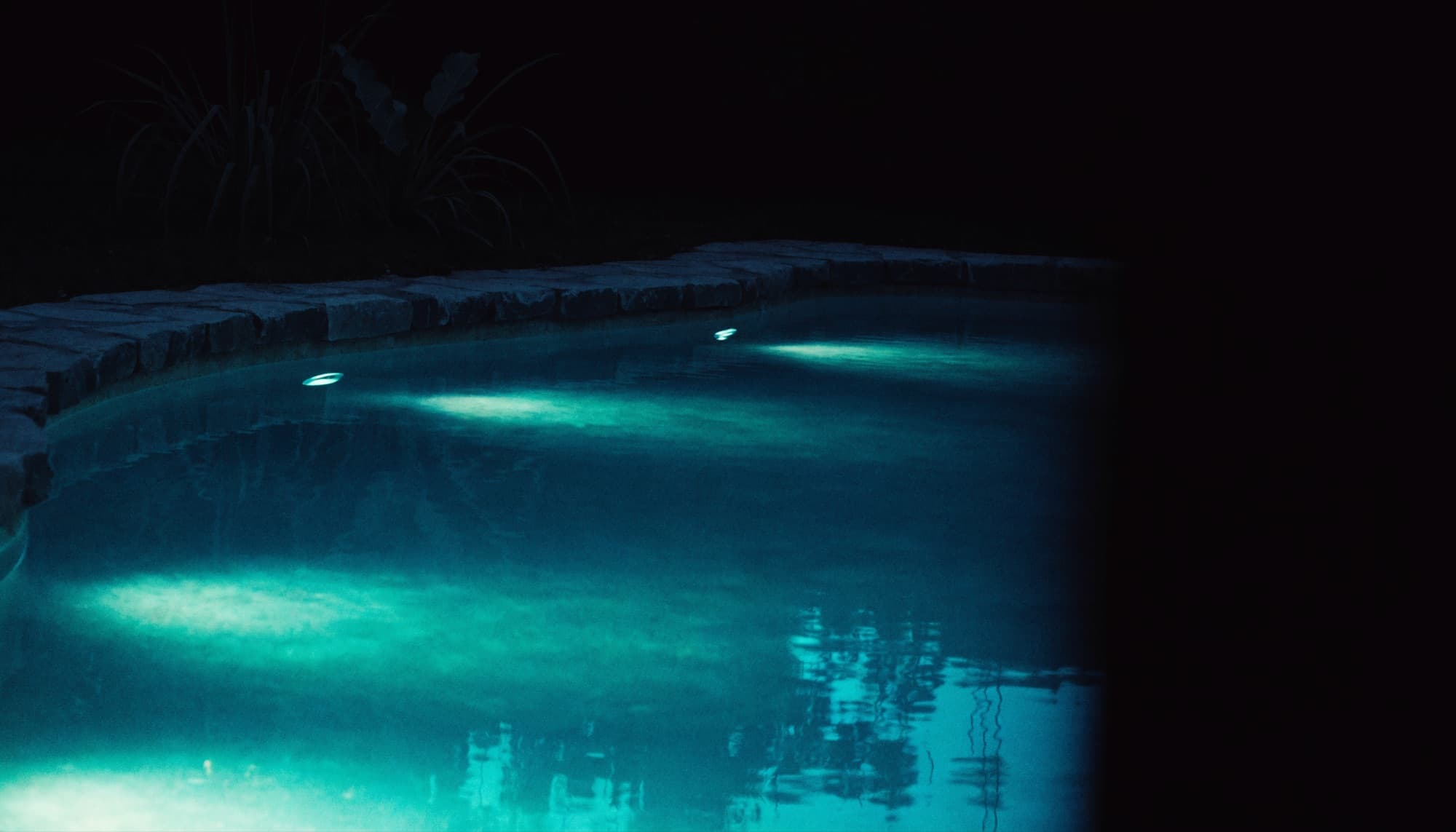 A backyard swimming pool lit turquoise at blue hour
