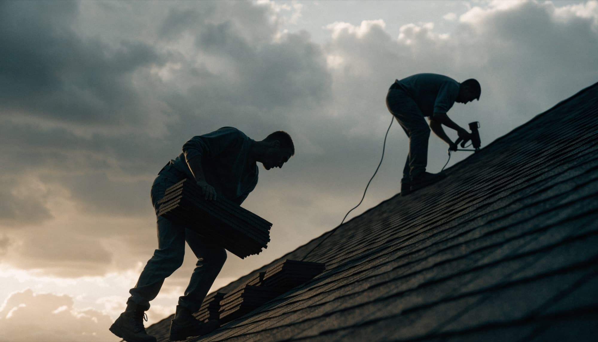Roofers installing shingles on a steep roof at golden hour