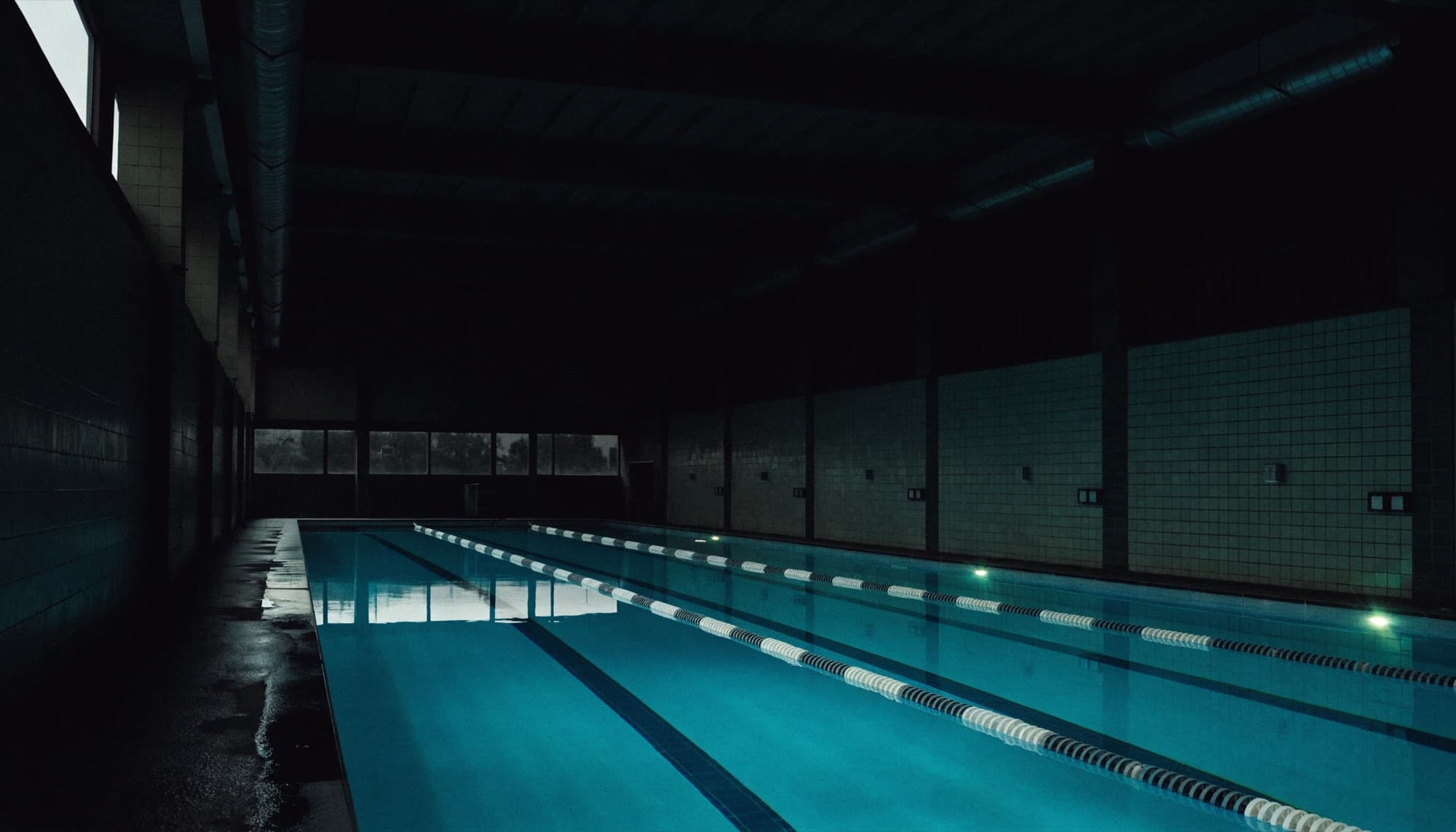 An indoor swimming pool at dawn with lane ropes and still water