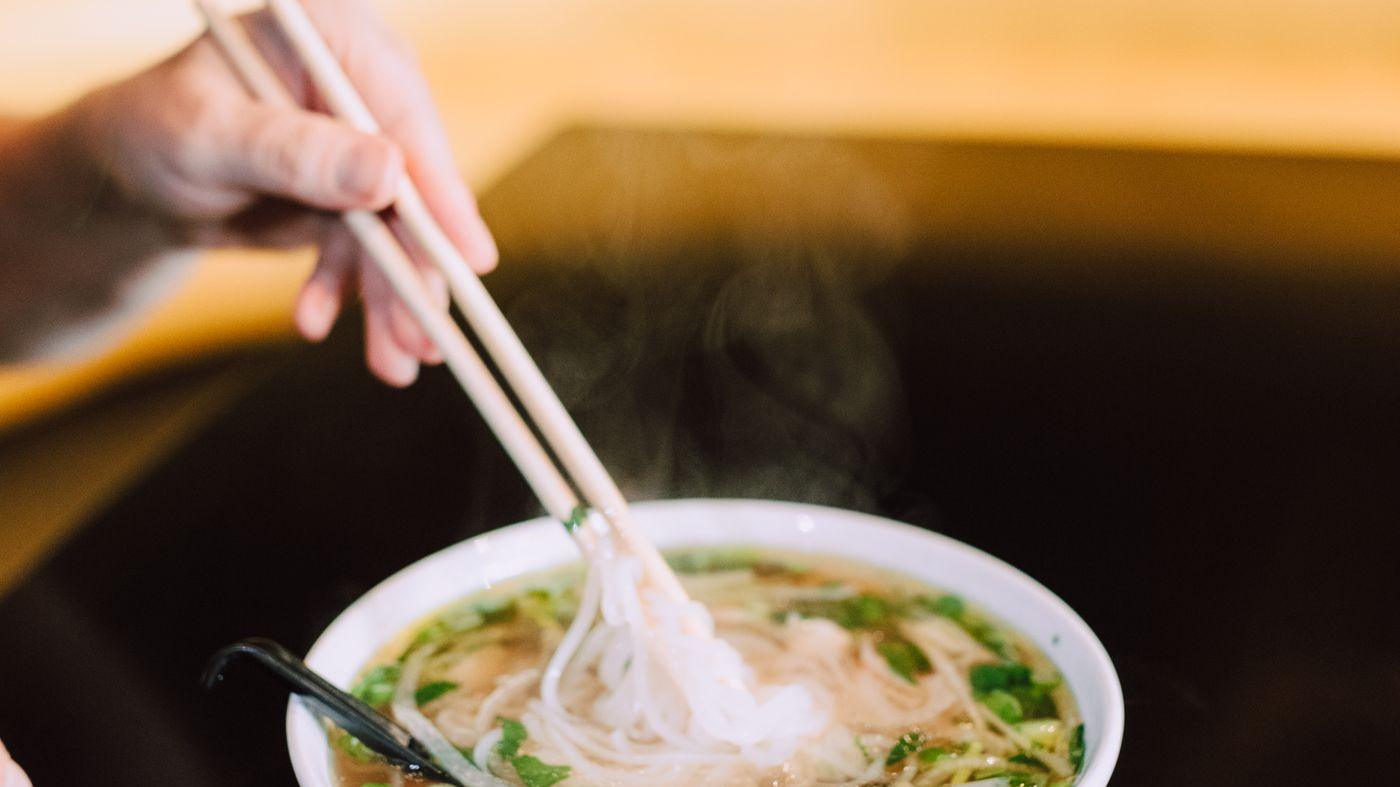 A bowl of pho lifted with chopsticks